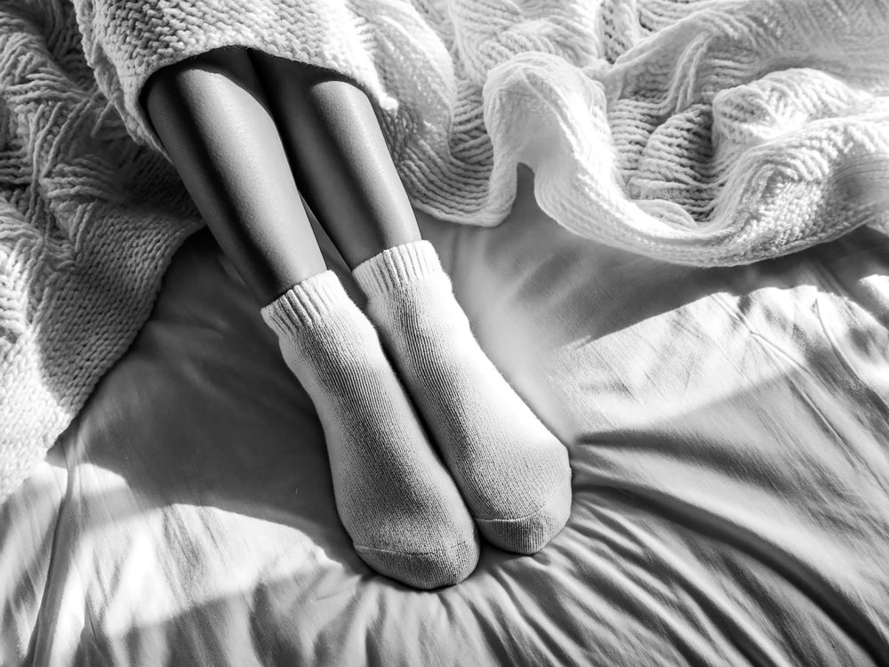 Eine Frau platziert ihre Füße in getragenen Socken auf einem Bett